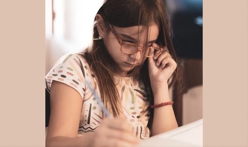 Bambina concentrata mentre scrive con una penna, simbolo di attenzione e apprendimento