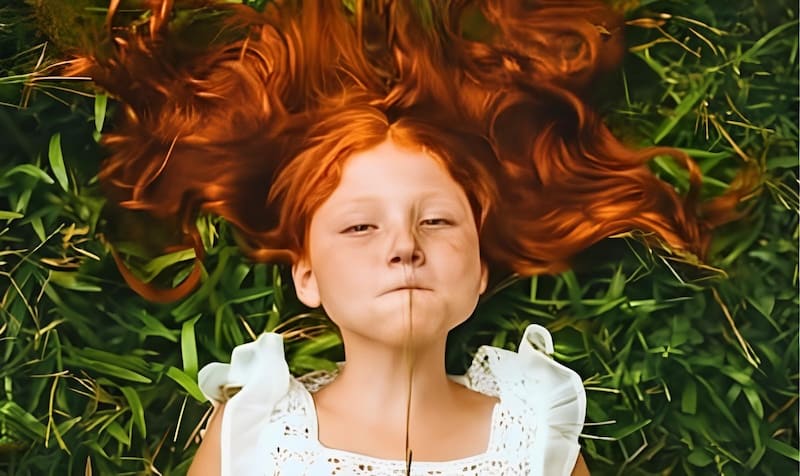 Bambina sul prato con espressione giocosa e curiosa durante un momento di relax all’aperto