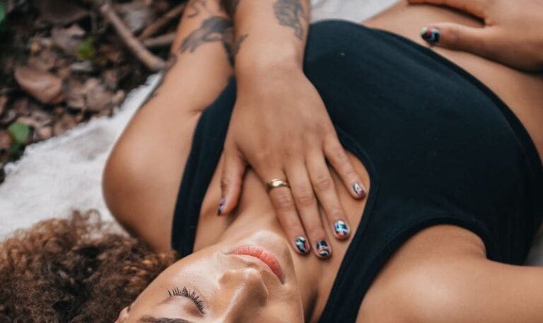 Donna sdraiata con gli occhi chiusi e le mani sul petto e sulla pancia, in un momento di ascolto e connessione con il proprio corpo