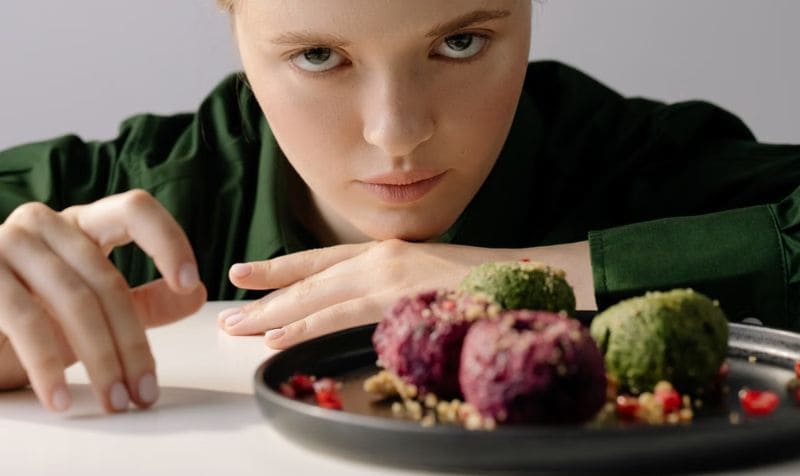 Ragazza con sguardo assente che fissa un piatto di cibo