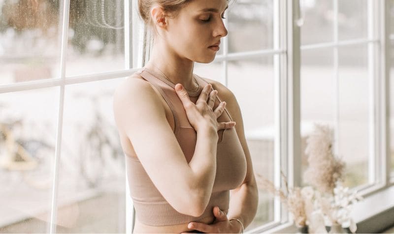 Ragazza seduta sul davanzale della cucina, con gli occhi chiusi e le mani sul petto e sulla pancia, in un momento di connessione con il proprio corpo
