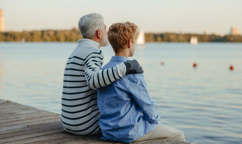 Adulto che tiene una mano sulla spalla di un ragazzo guardando il lago in silenzio