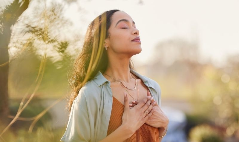 Donna con gli occhi chiusi, le mani sul cuore e un viso rilassato in un momento di respiro consapevole