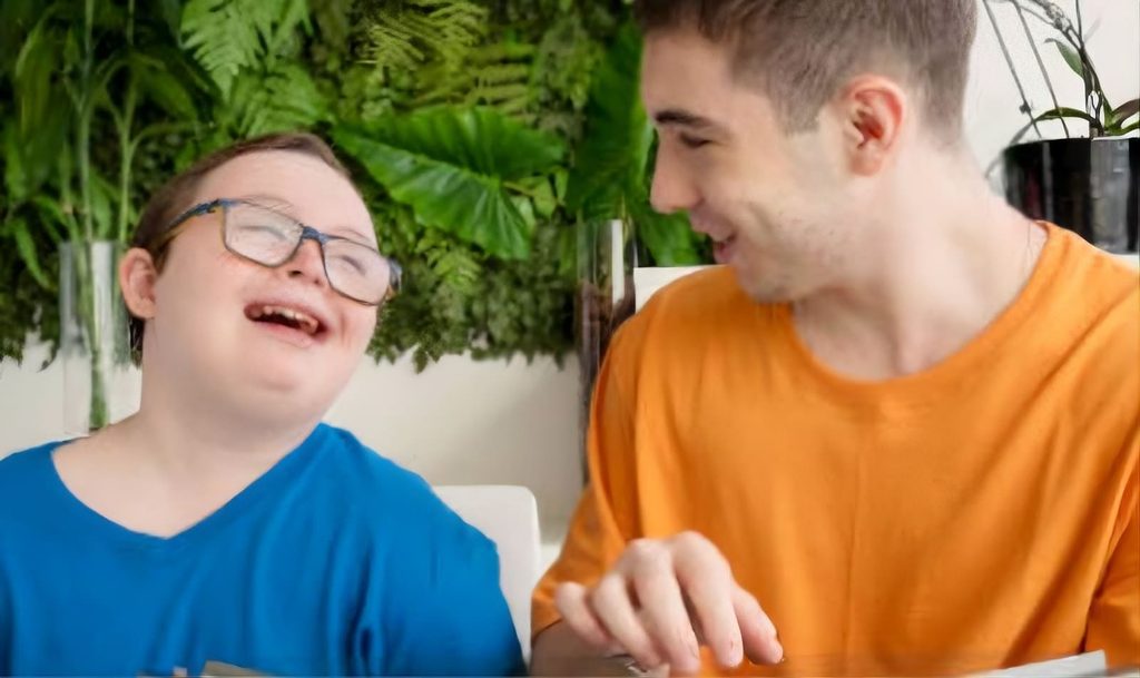 Ragazzo con sindrome di down che ride felice di fianco all'insegnante in una stanza con delle piante
